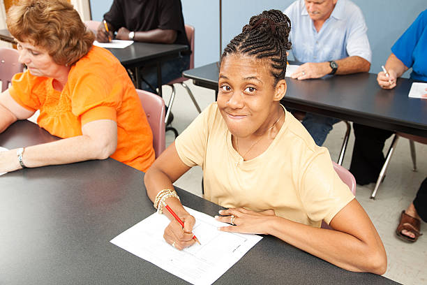 An African American woman with CP in a yellow shirt and braids is seated at a desk.   

