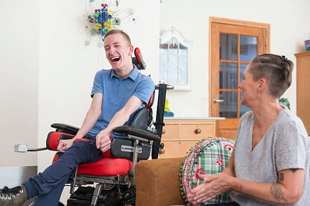White man with ALS sitting in chair laughing. White woman sitting beside him laughing as well
